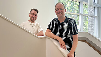 Marian Antoni und Heiko Hauger stehen auf einer Treppe und lächeln